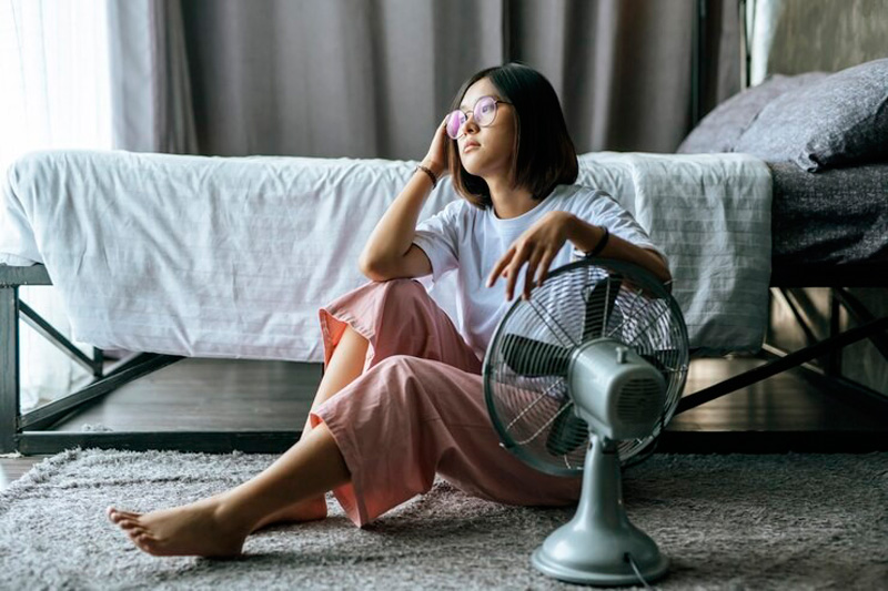 Mujer joven sentada al lado de un ventilador